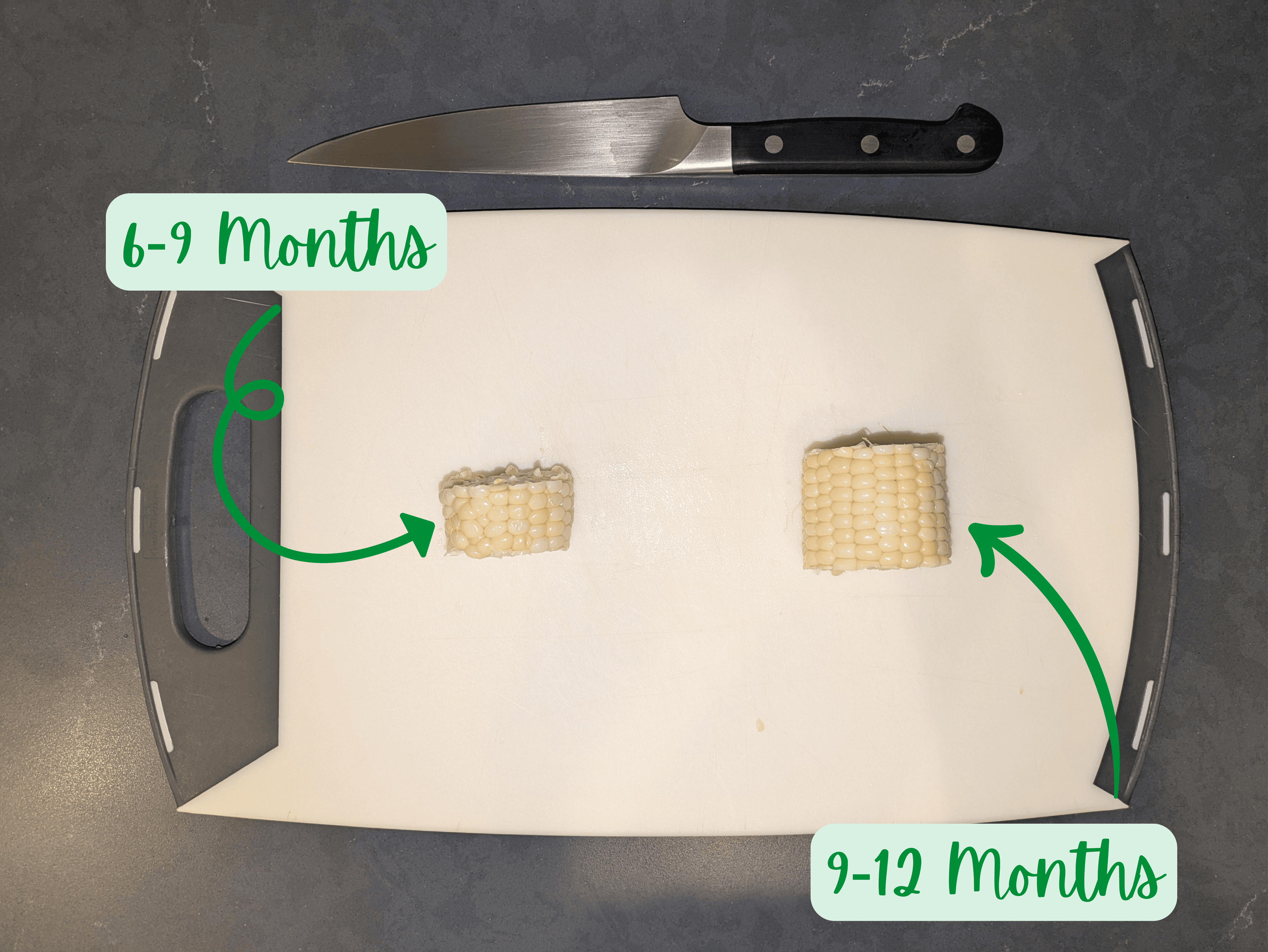 A photograph of a cutting board on a dark counter with 2 different size pieces of corn on the cob